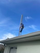 Person climbing a metal communications tower on a building roof, under a blue sky.