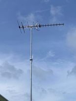 A tall, silver outdoor TV antenna against a partly cloudy, blue sky.