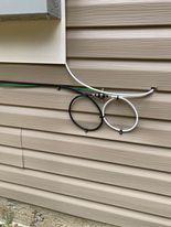 White and black cables looping on tan siding, near a white box.