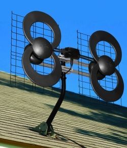 Black antenna with four circular elements and a mesh reflector, mounted on a roof.