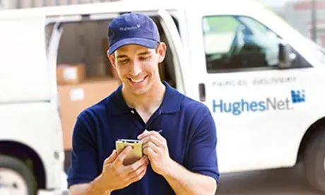 Delivery person with HughesNet van, smiling and using a smartphone.