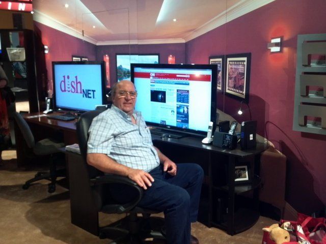 Man sitting in a room with two large screens, one showing