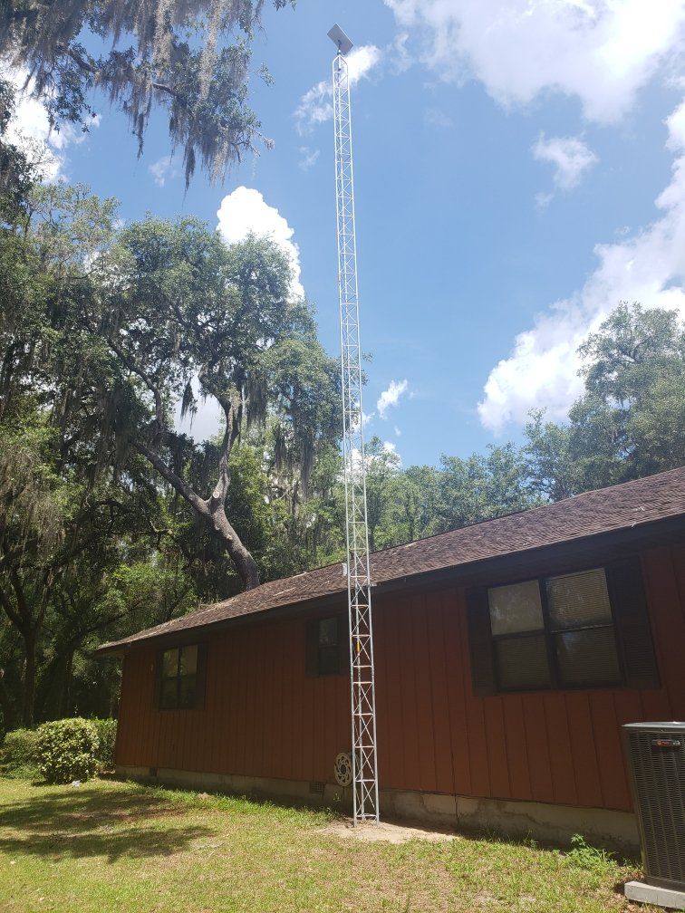 A tall, metal communication tower next to a reddish-brown house under a partly cloudy sky.