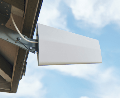 White directional antenna mounted under roof overhang against a cloudy sky.