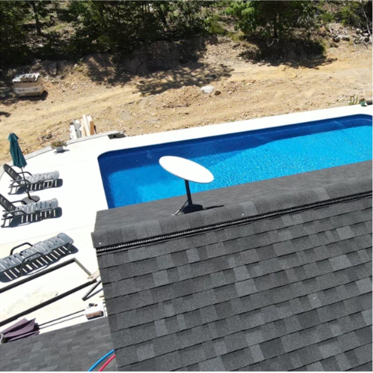 Satellite dish on a roof overlooking a pool with lounge chairs, trees, and construction.