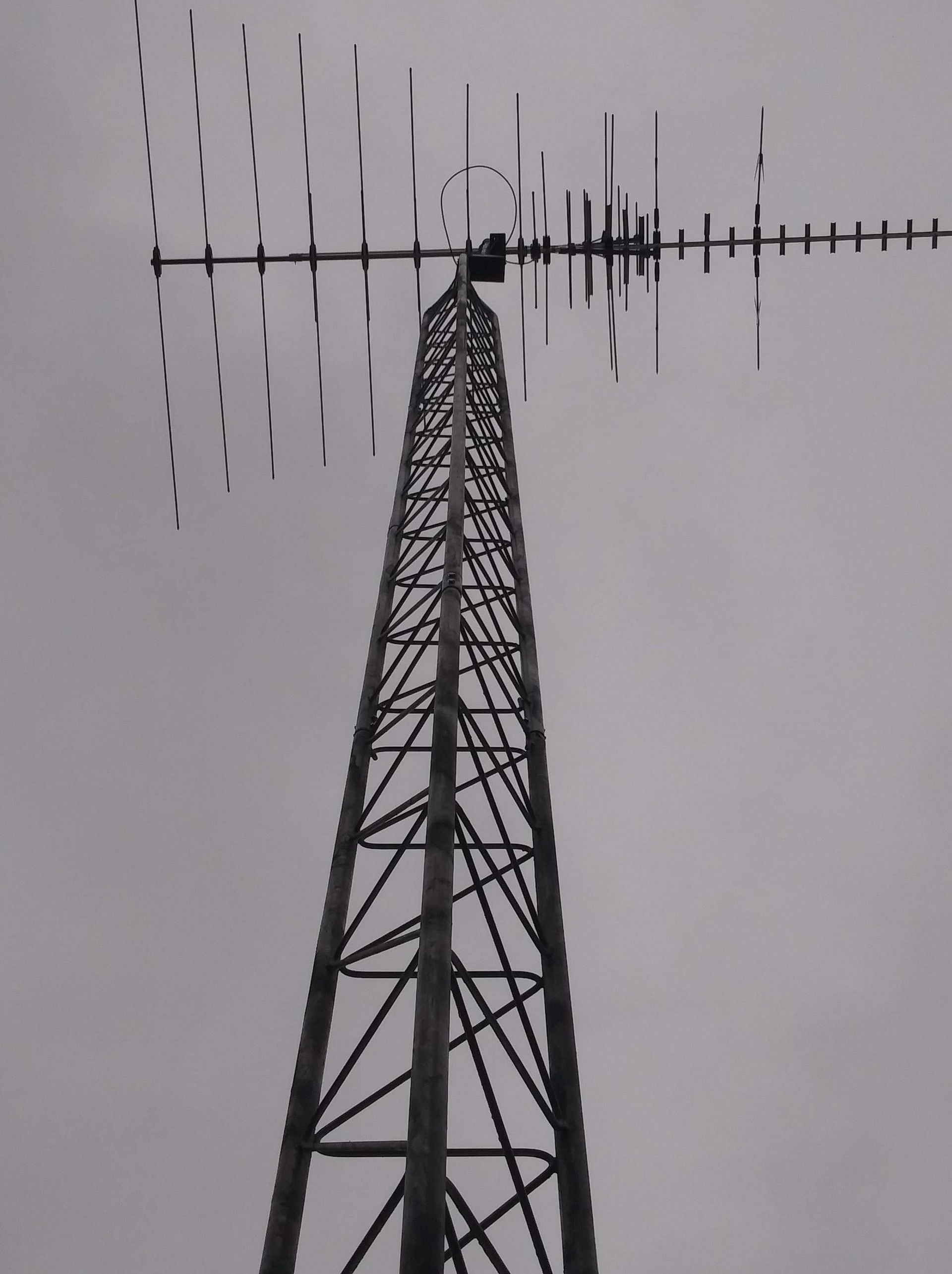 Tall metal antenna tower against a cloudy sky, with multiple horizontal antenna arrays.