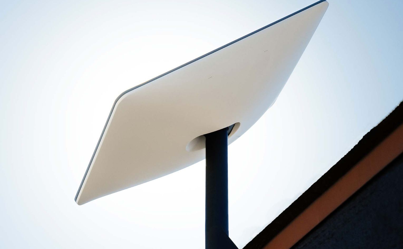 White Starlink satellite dish on black pole against a blue sky.