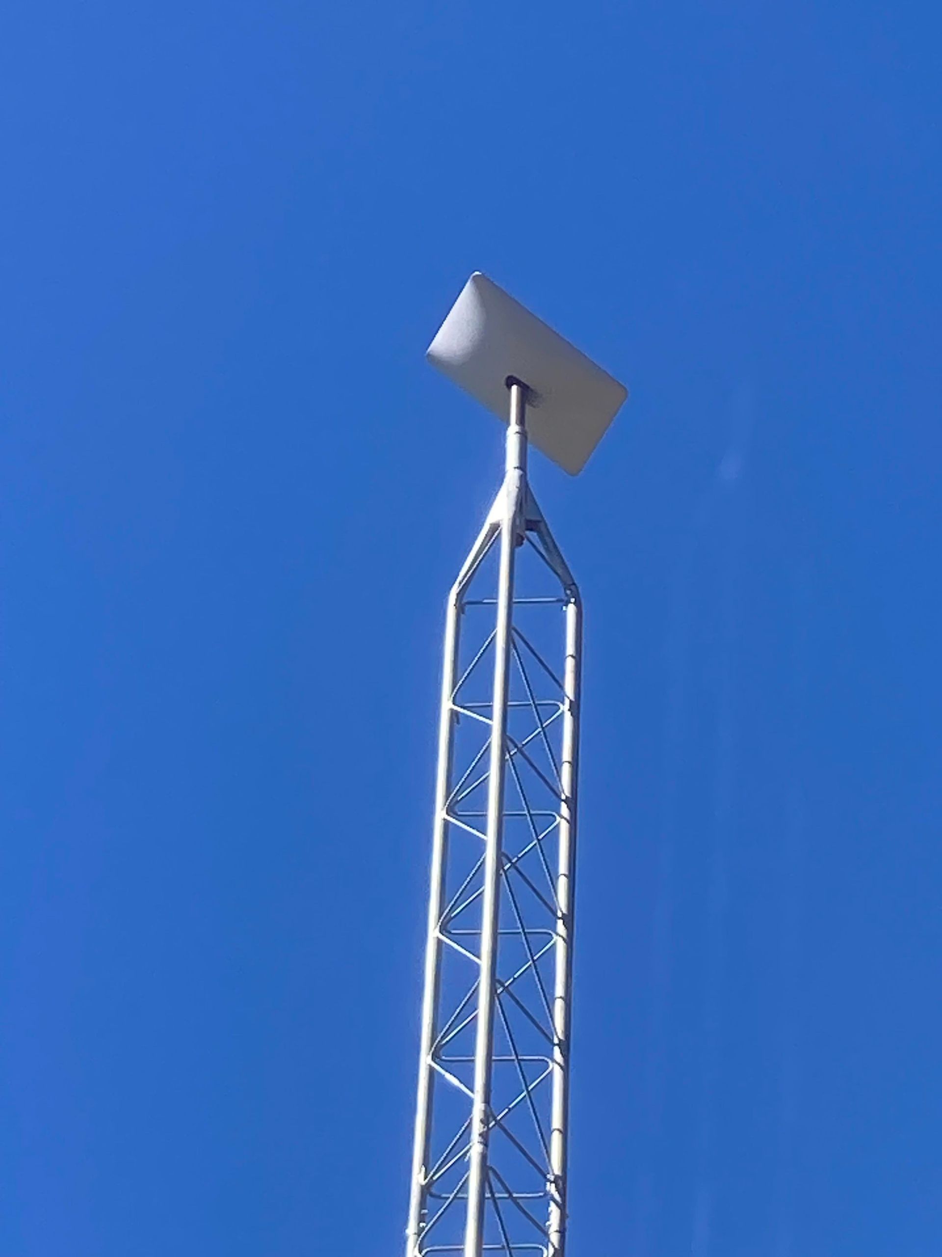 White radio tower against a bright blue sky. Rectangular antenna at top.