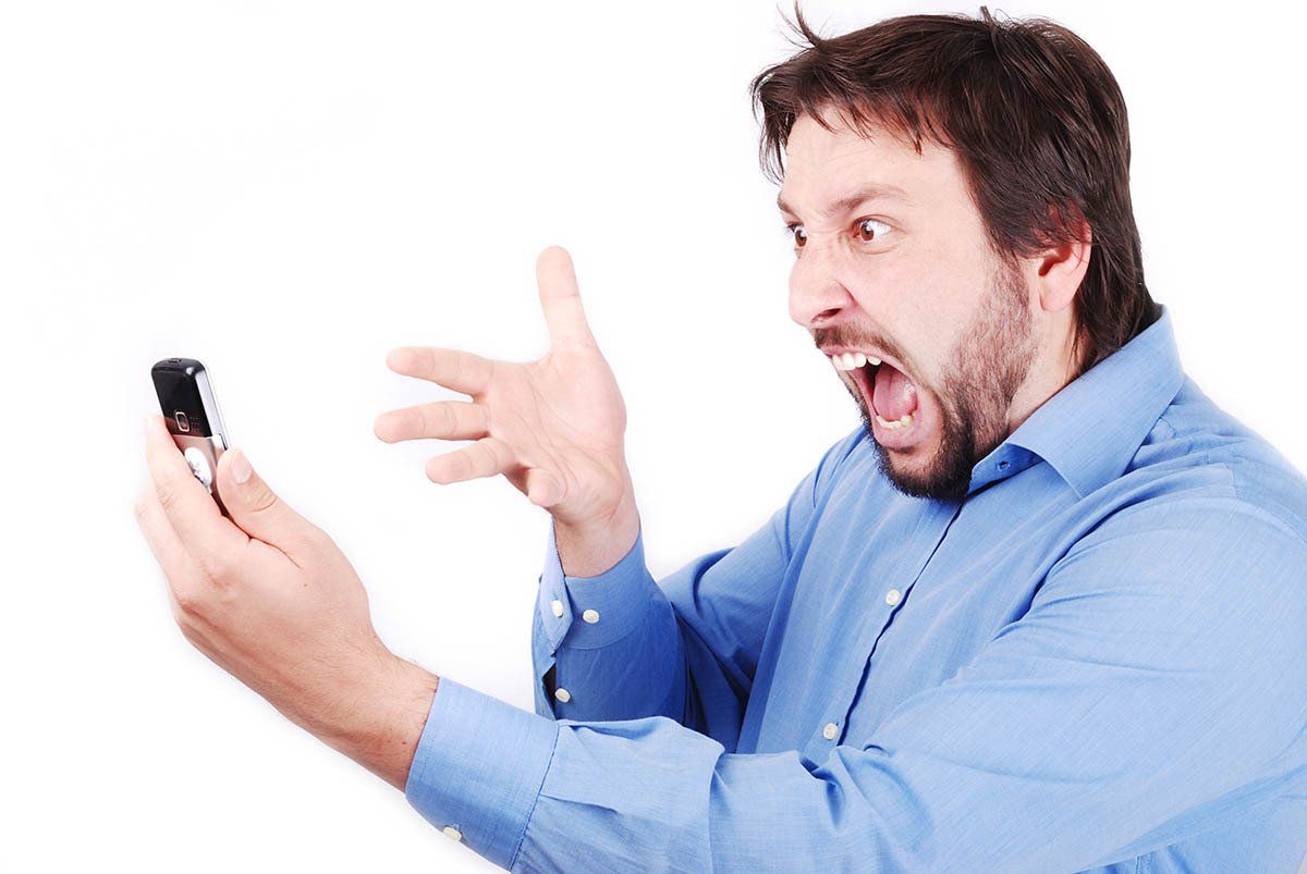 Man in blue shirt angrily shouting at a smartphone against a white background