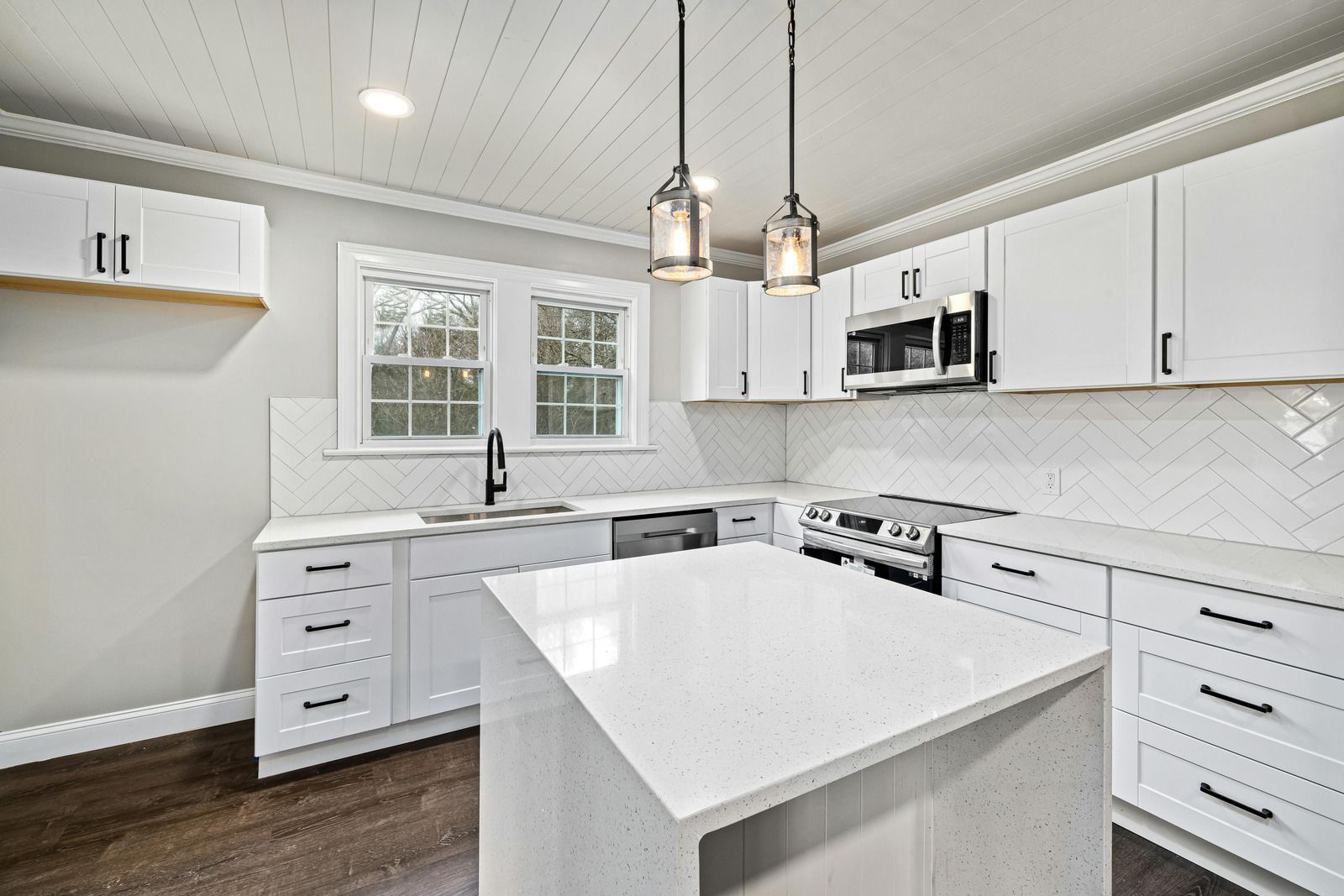 Modern white kitchen with island, stainless appliances, pendant lights, and dark wood floors
