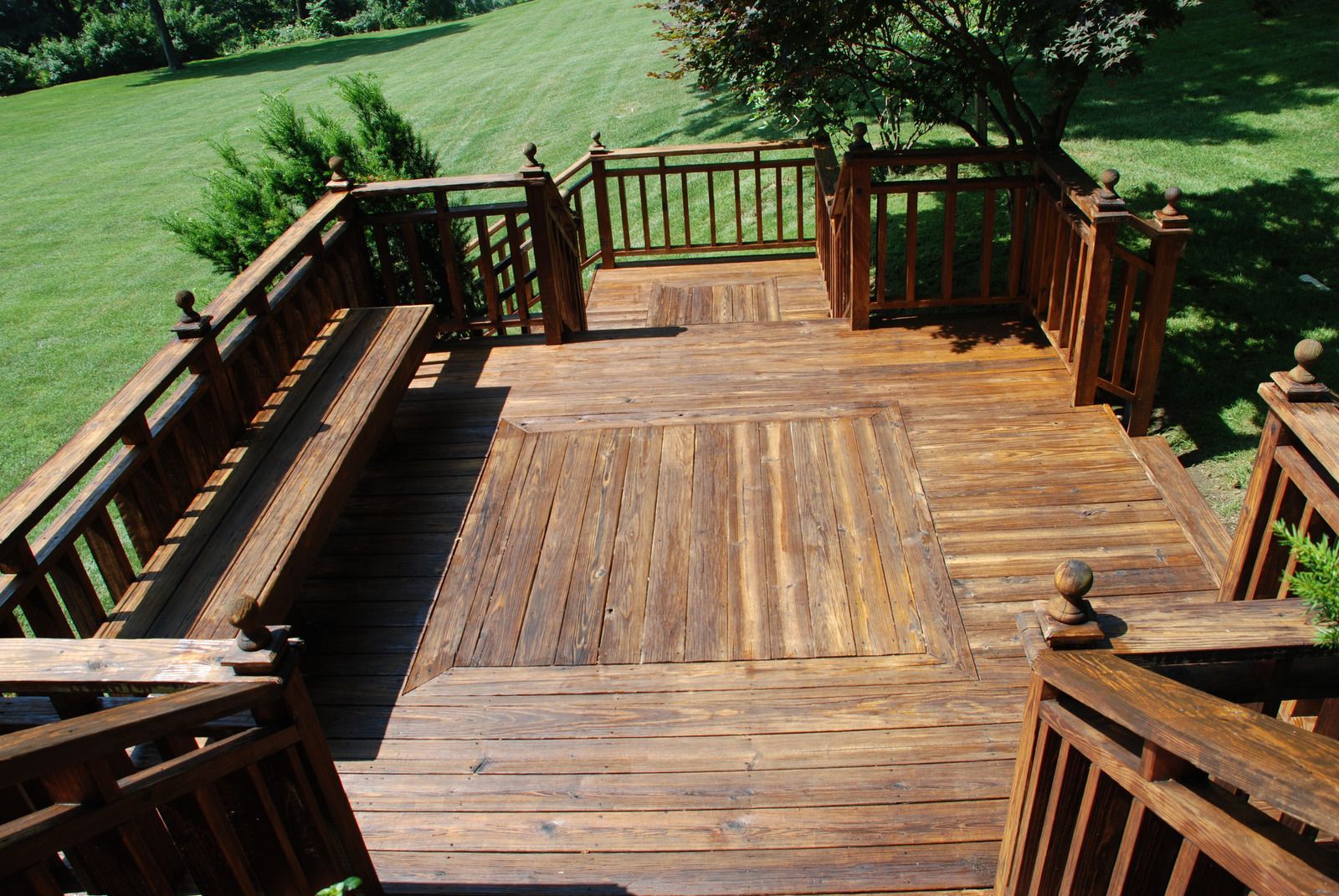 Wooden deck overlooking a green lawn, with benches and railings in bright sunlight.