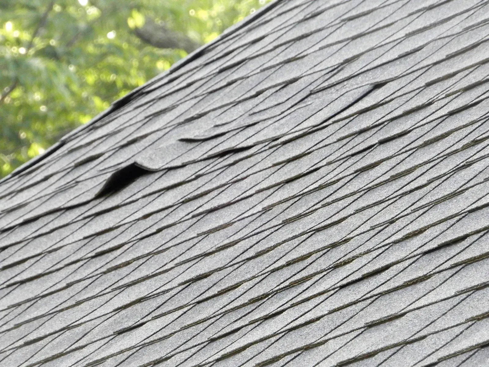 Worker using a nail gun to install roofing shingles on a roof