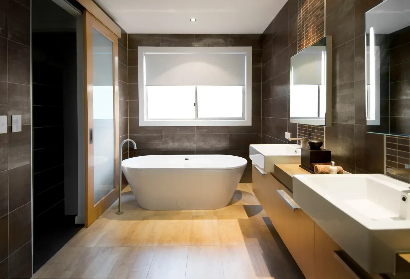 Modern bathroom with freestanding tub, double sinks, large window, and dark tiled walls