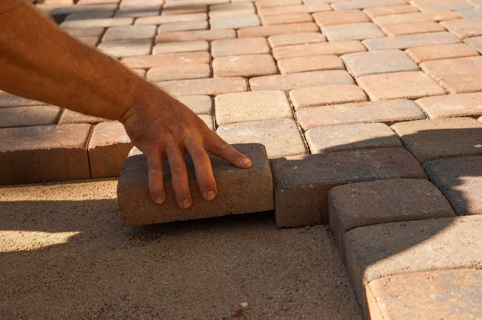 Hand placing a paving stone into a brick patio beside a border