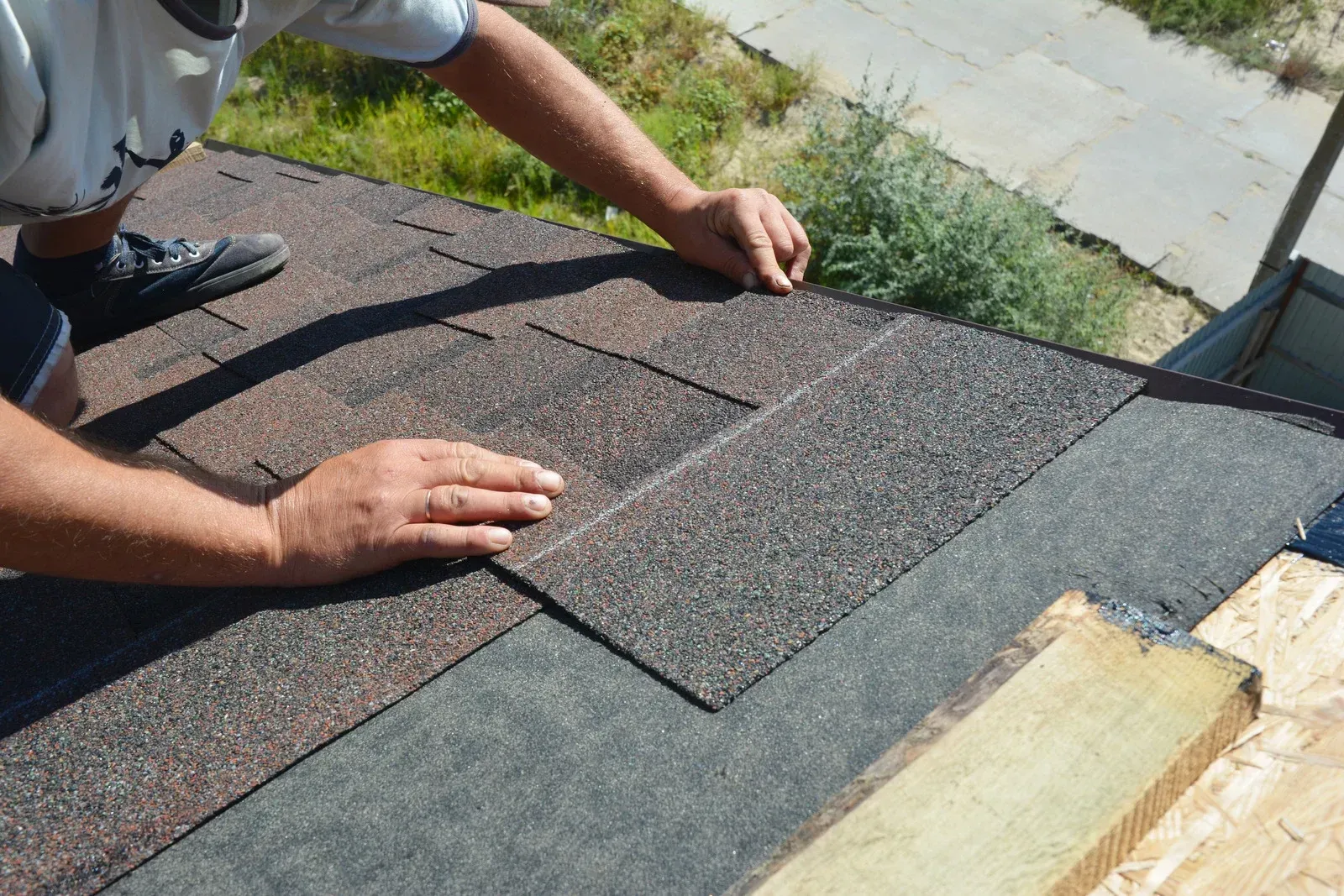 Person installing dark asphalt shingles on a roof, with hands placing a new shingle row.