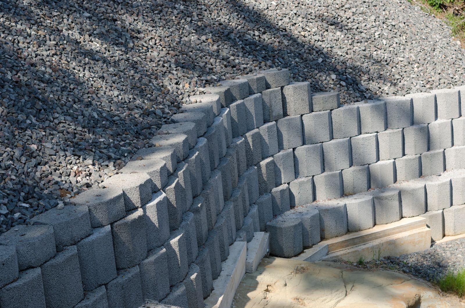 Terraced gray retaining wall curving along a gravel slope beside a sandy area