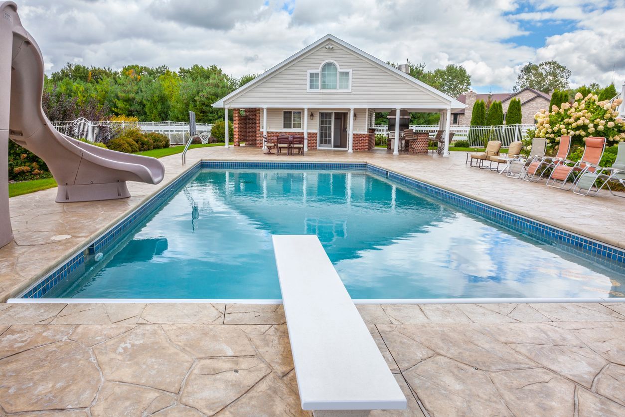 A large swimming pool with a slide and a diving board in front of a house.