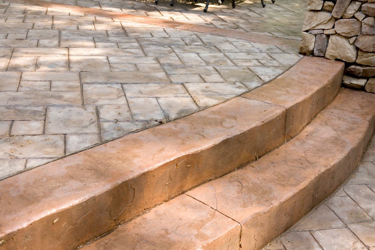 A set of concrete steps leading up to a stone patio.