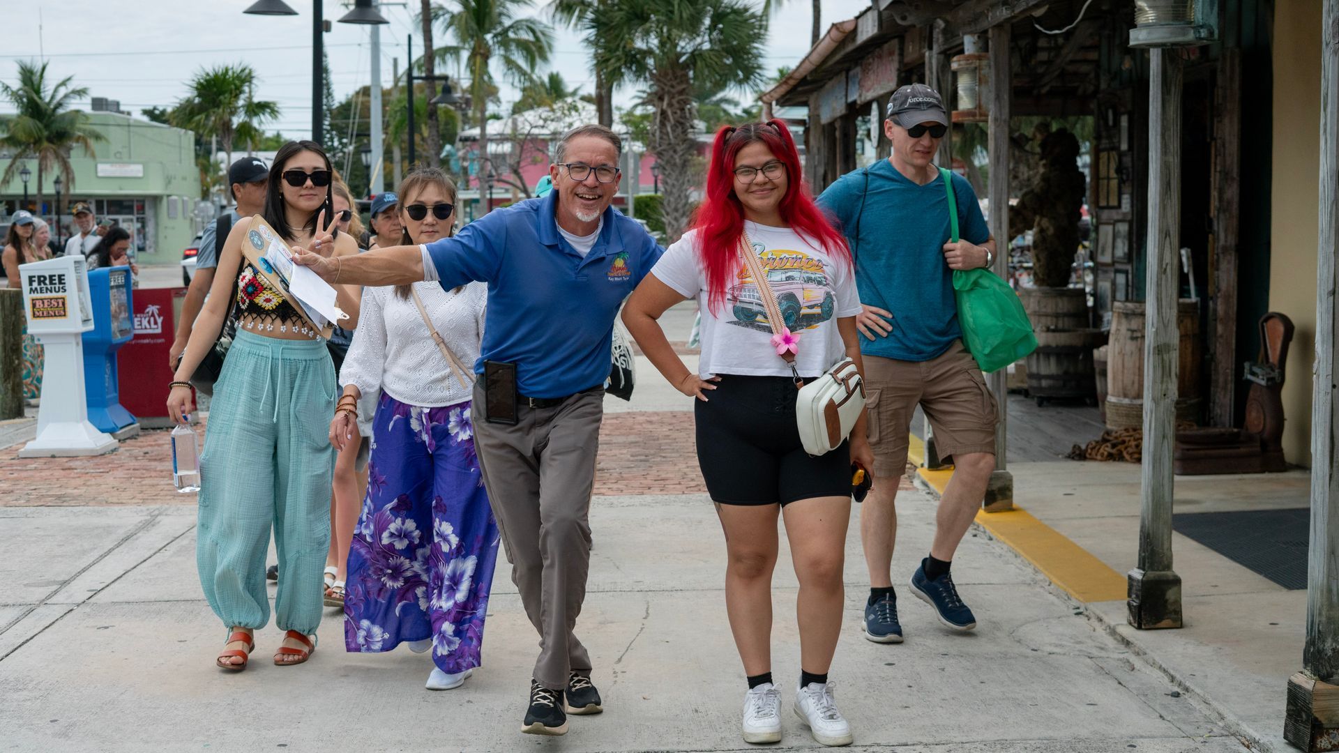 Tour guide cheerfully leading a diverse group of tourists through a lively street lined with shops and palm trees in Key West, Florida.