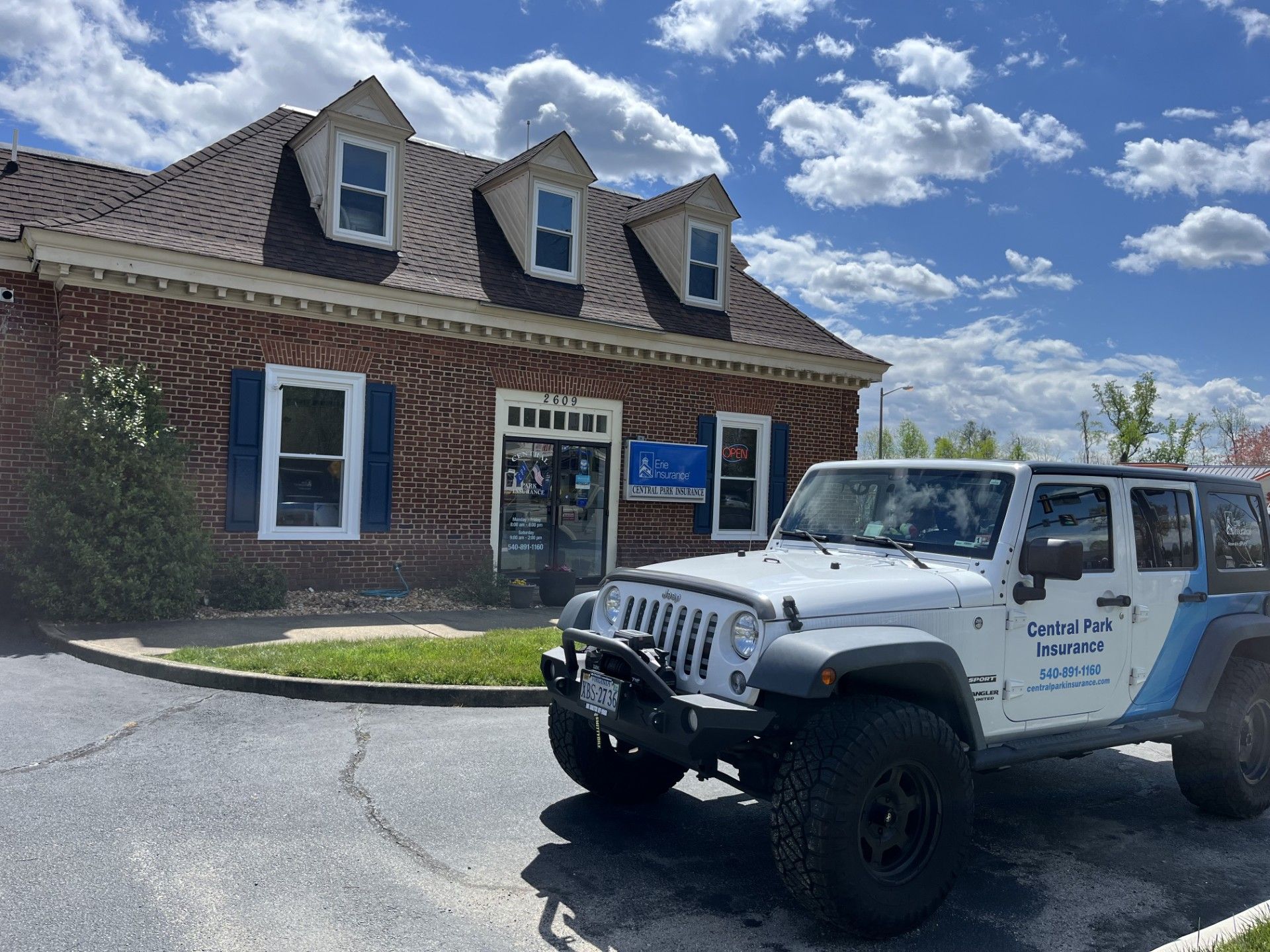 White Jeep parked outside a brick building with dormer windows under a bright blue sky
