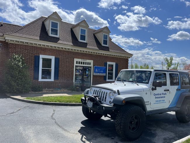 White Jeep parked outside a brick building with dormer windows under a bright blue sky