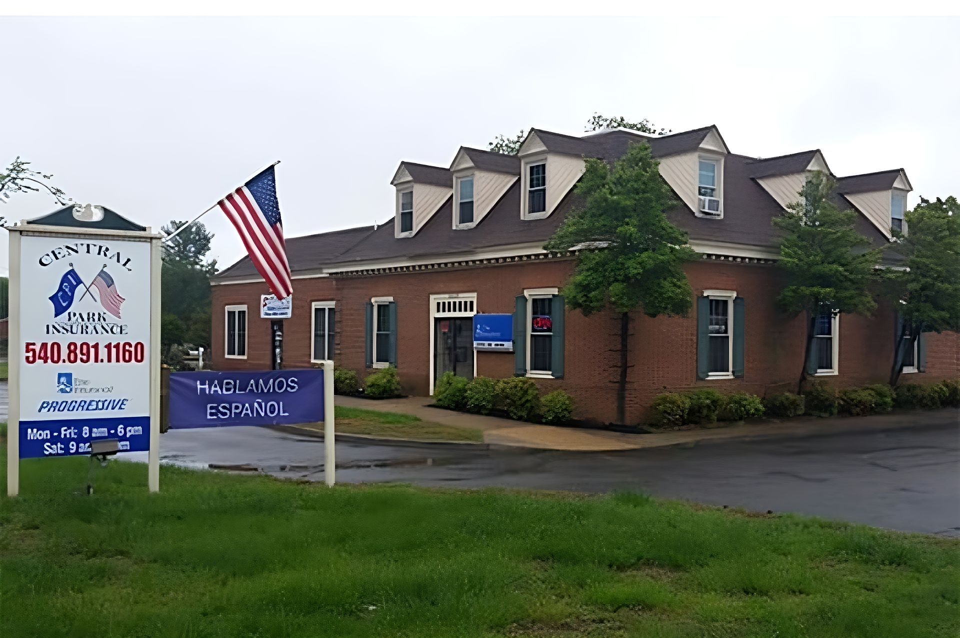 Brick chiropractic office with sign and American flag beside a grassy roadside.