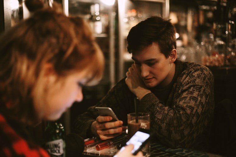 A man and a woman are sitting at a table looking at their phones.