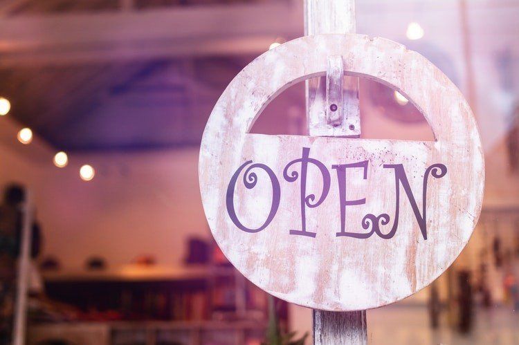 A wooden open sign is hanging in a store window.