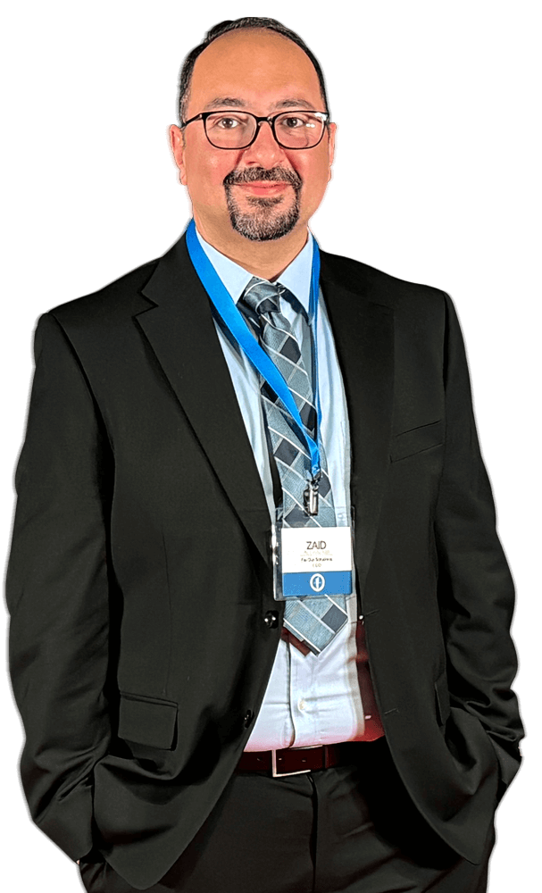 Man in a black suit with blue tie and conference badge standing against a white background