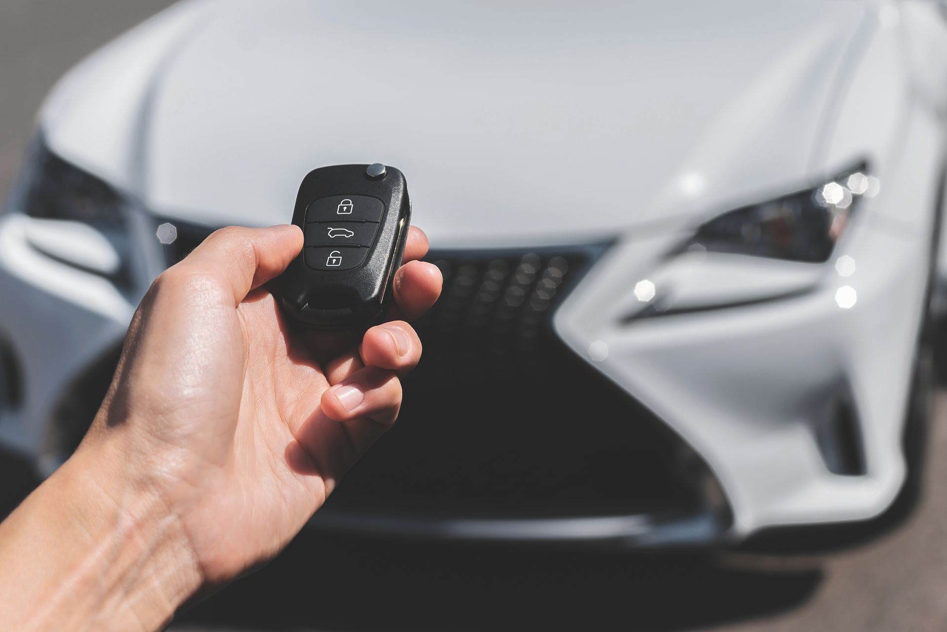 Hand holding a car fob key while standing in front of a white vehicle. Hand holding a car fob key while standing in front of a white vehicle.