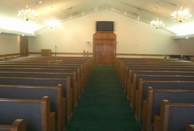 Empty church sanctuary with wooden pews, green carpeted aisle, and a pulpit at the front