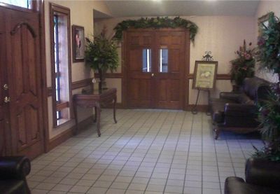 Lobby with tiled floor, double wooden doors, chairs, and greenery around the entrance.