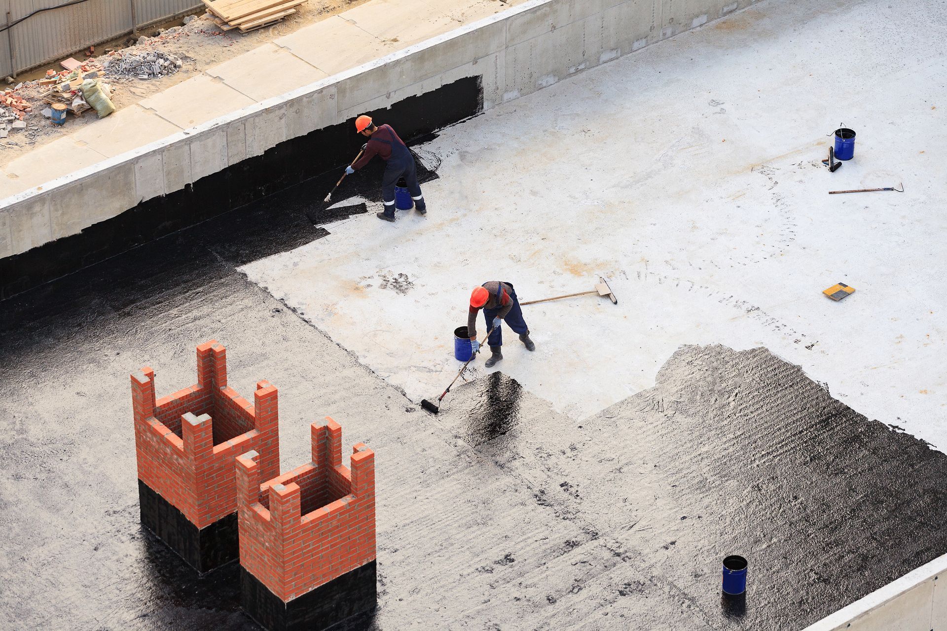 Workers paving a roadway beside a partially built brick structure and concrete curb