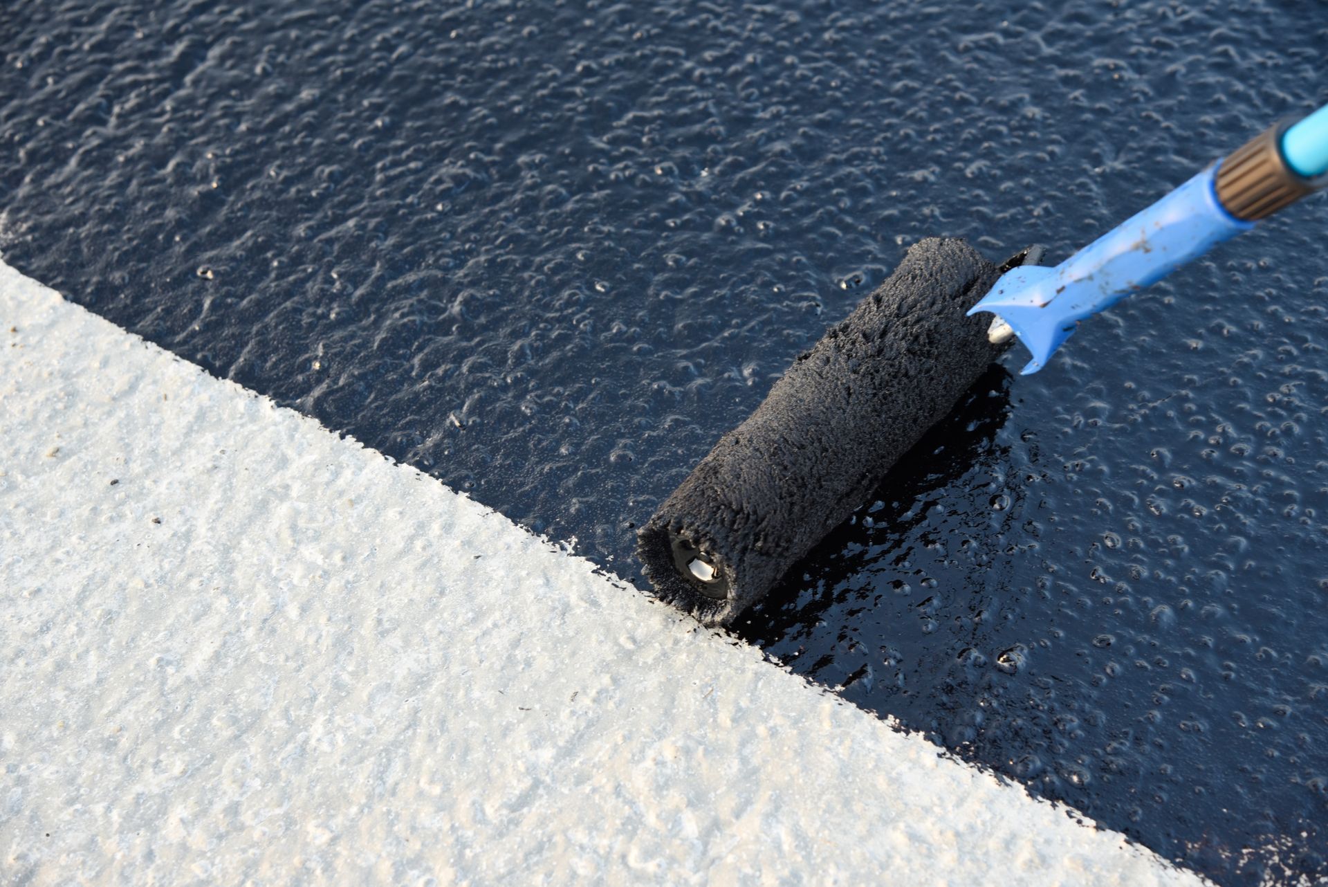 Paint roller applying white coating over a dark textured surface