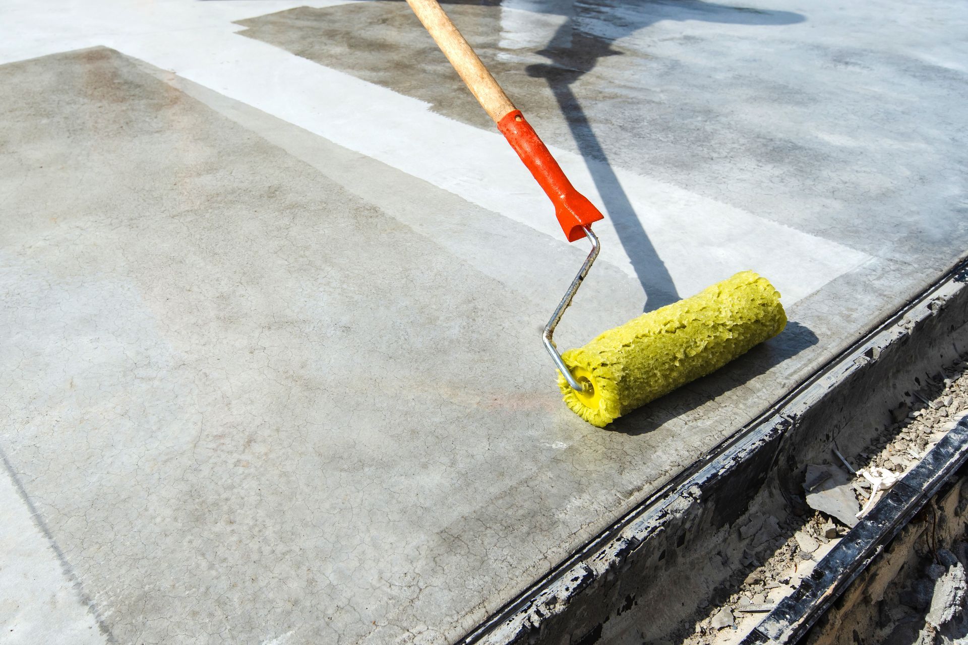 Yellow paint roller applying coating to a concrete floor edge outdoors