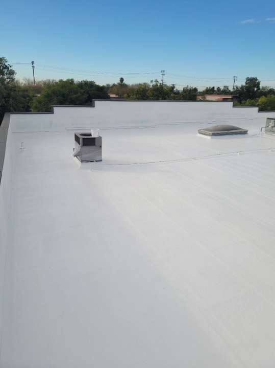 White flat rooftop with two vents under a clear blue sky.
