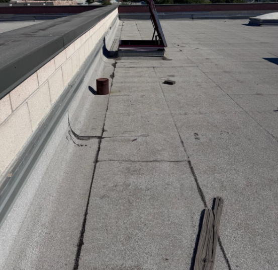 Flat rooftop with white membrane, vents, and a raised edge under bright sunlight