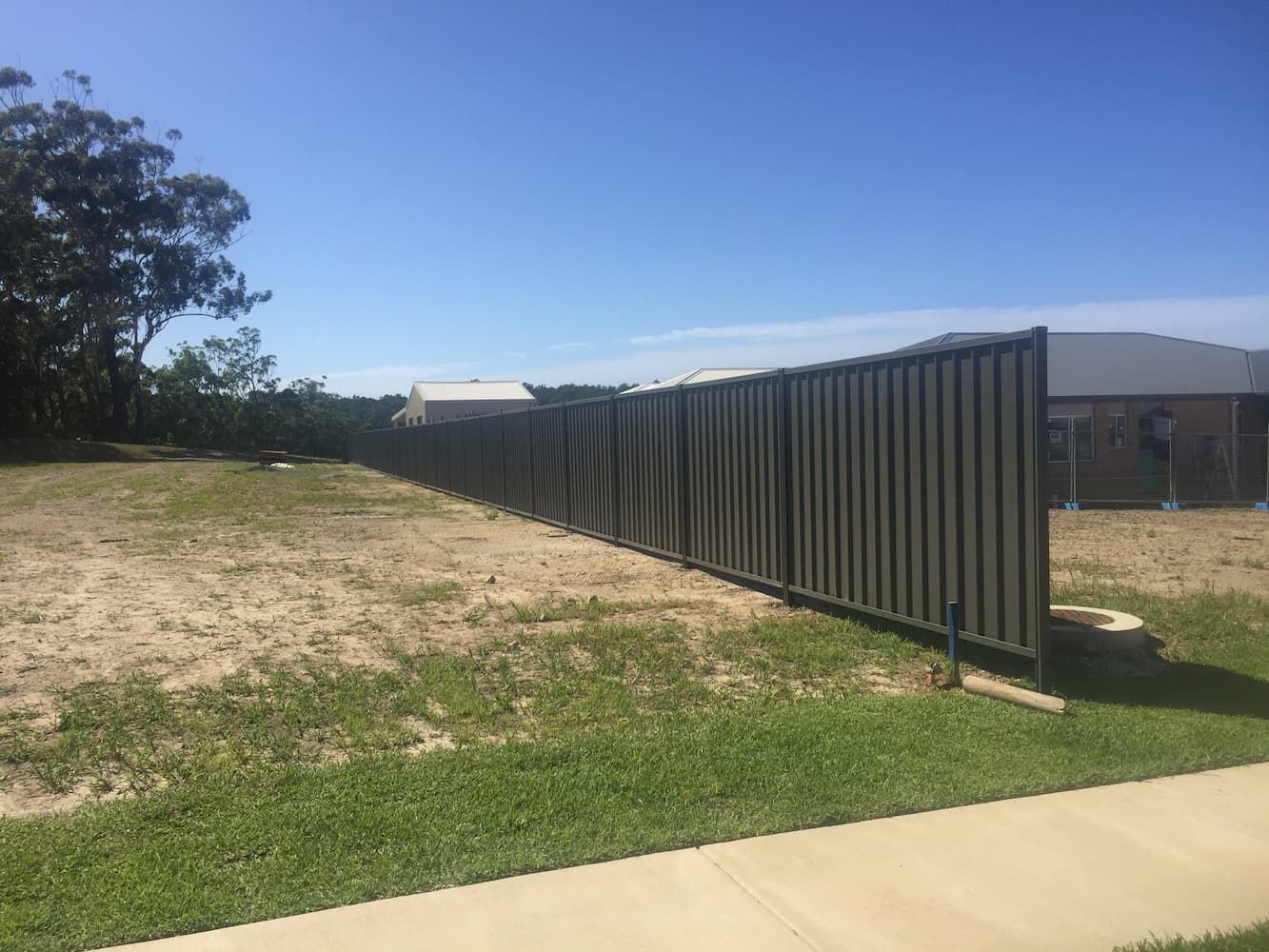 A Fence is Surrounding a Grassy Field Next to a Sidewalk — Harbour Fencing In Moonee Beach, NSW