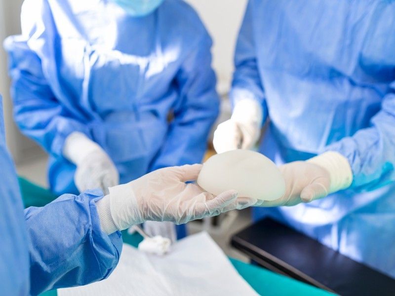 Um cirurgião segura um implante mamário na mão em uma sala de cirurgia.