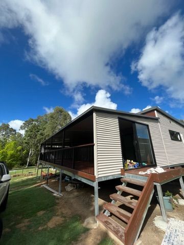 Elevated beige home with a deck and stairs, set against a blue sky with clouds and green grass — Steel Homes Australia in Branyan, QLD