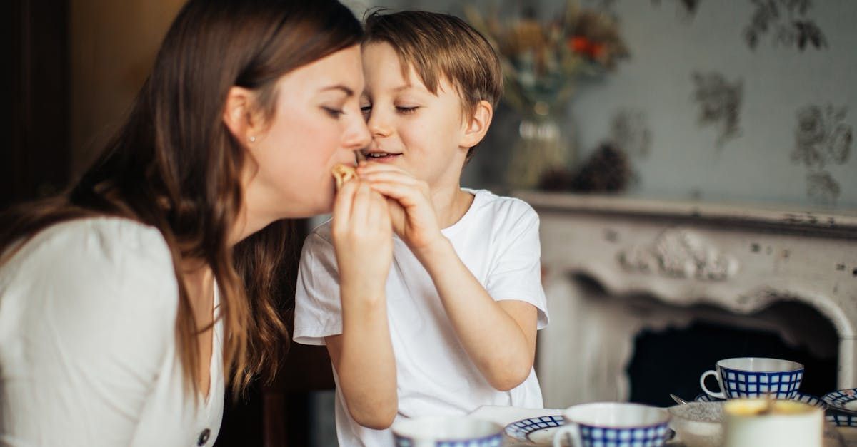 Woman and young boy sharing a cookie, close together at a table.