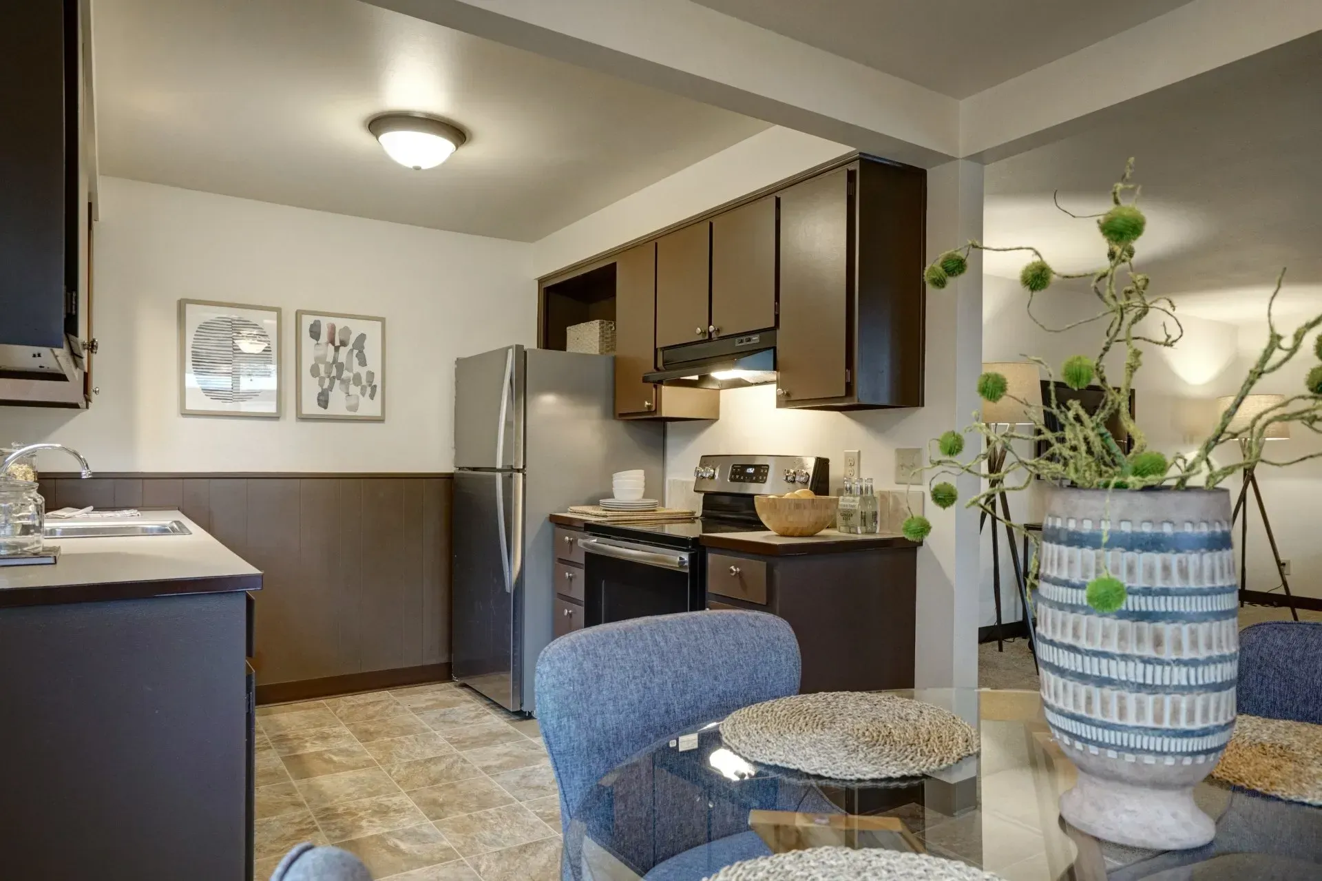 Kitchen with brown cabinets, stainless steel appliances, and a table with a blue chair.