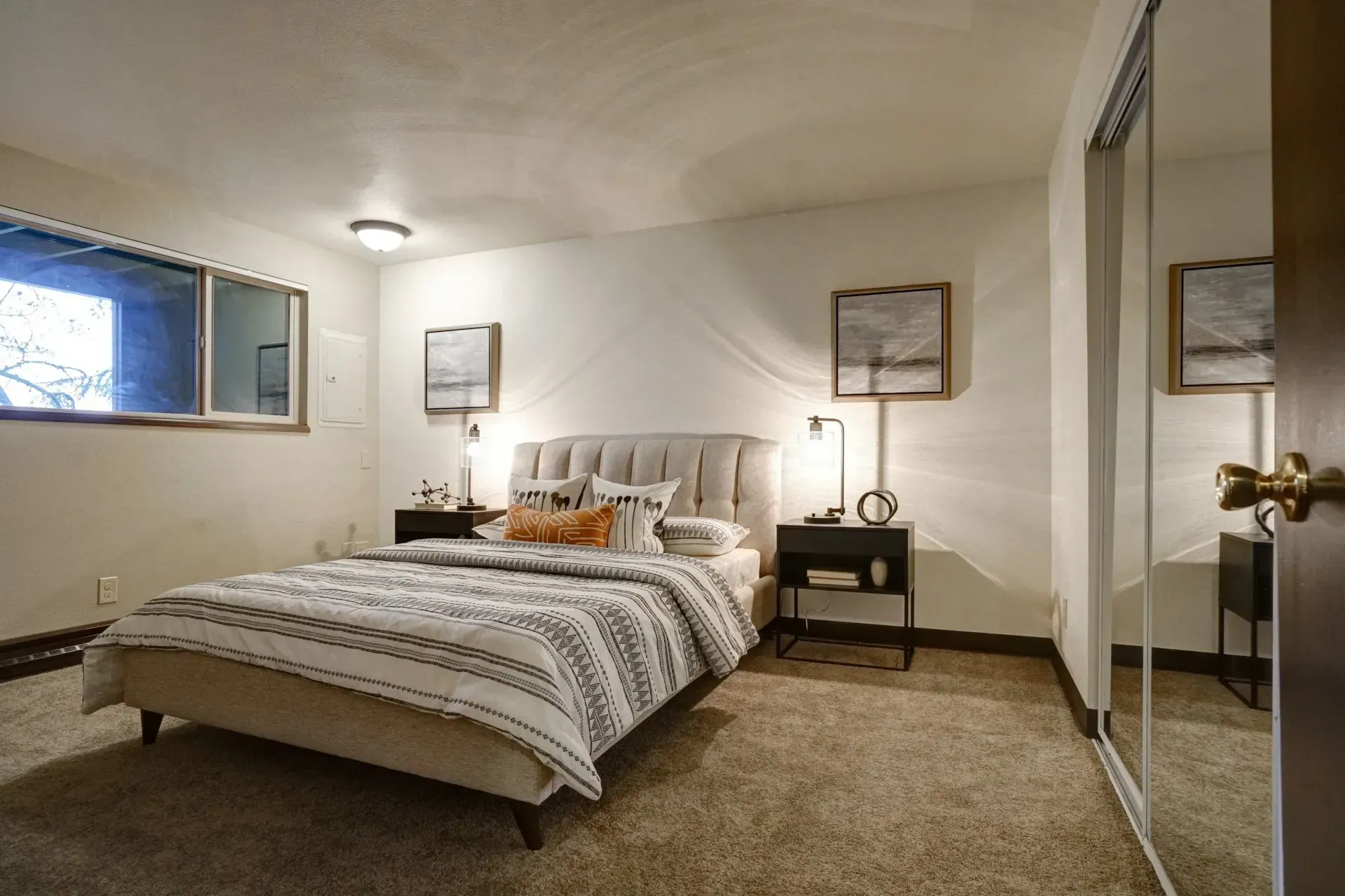 Bedroom with a bed, nightstands, artwork, large mirrored closet, and a window.