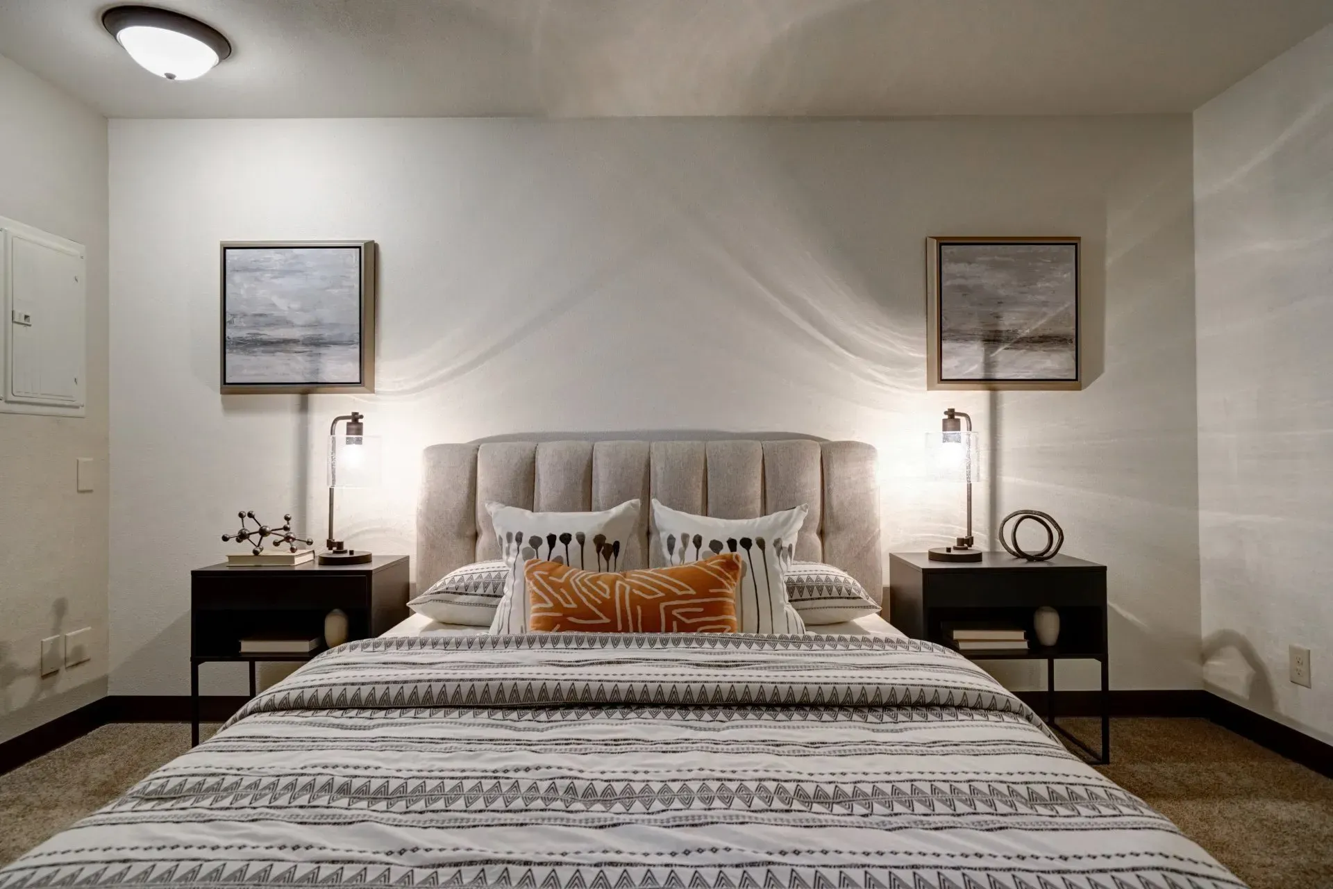 Bedroom with upholstered headboard, art prints, nightstands, lamps, and patterned bedding.