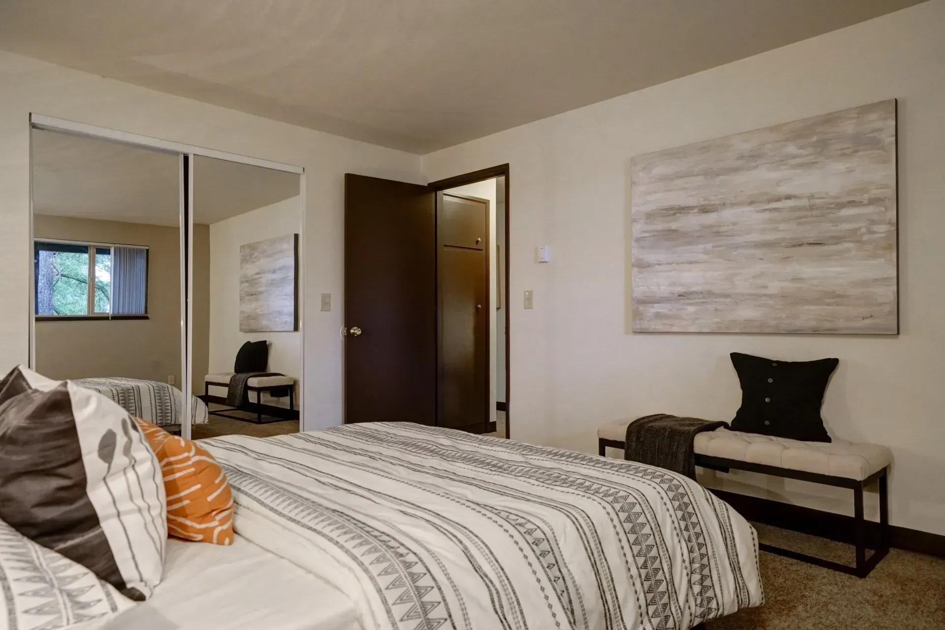 Bedroom with bed, mirrored closet, abstract art, and bench.