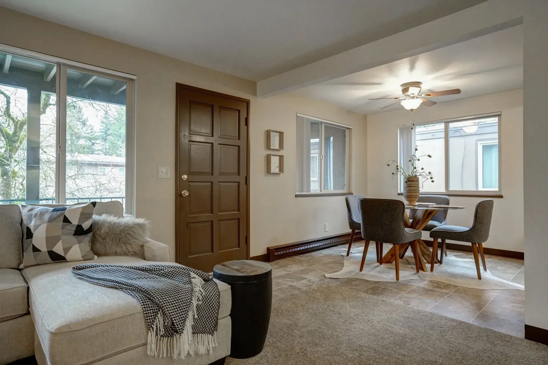 Beige living room with sectional sofa, dining area with round table, and a brown door.