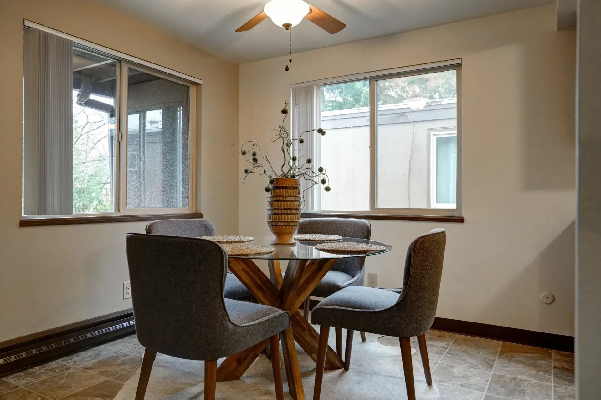 Dining room with a glass table, four gray chairs, and a decorative vase.