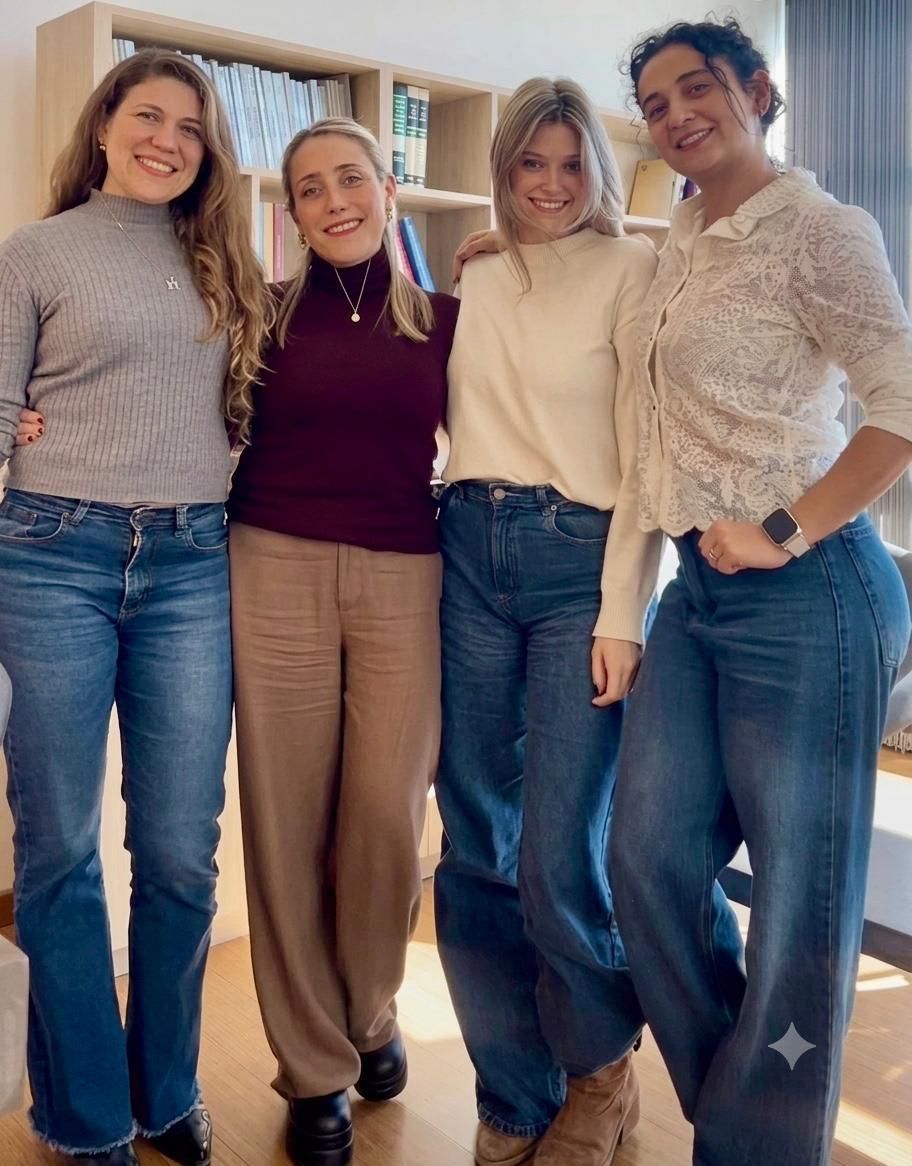 Cuatro personas de pie en el interior, sonriendo y posando juntas cerca de una ventana y una mesa.