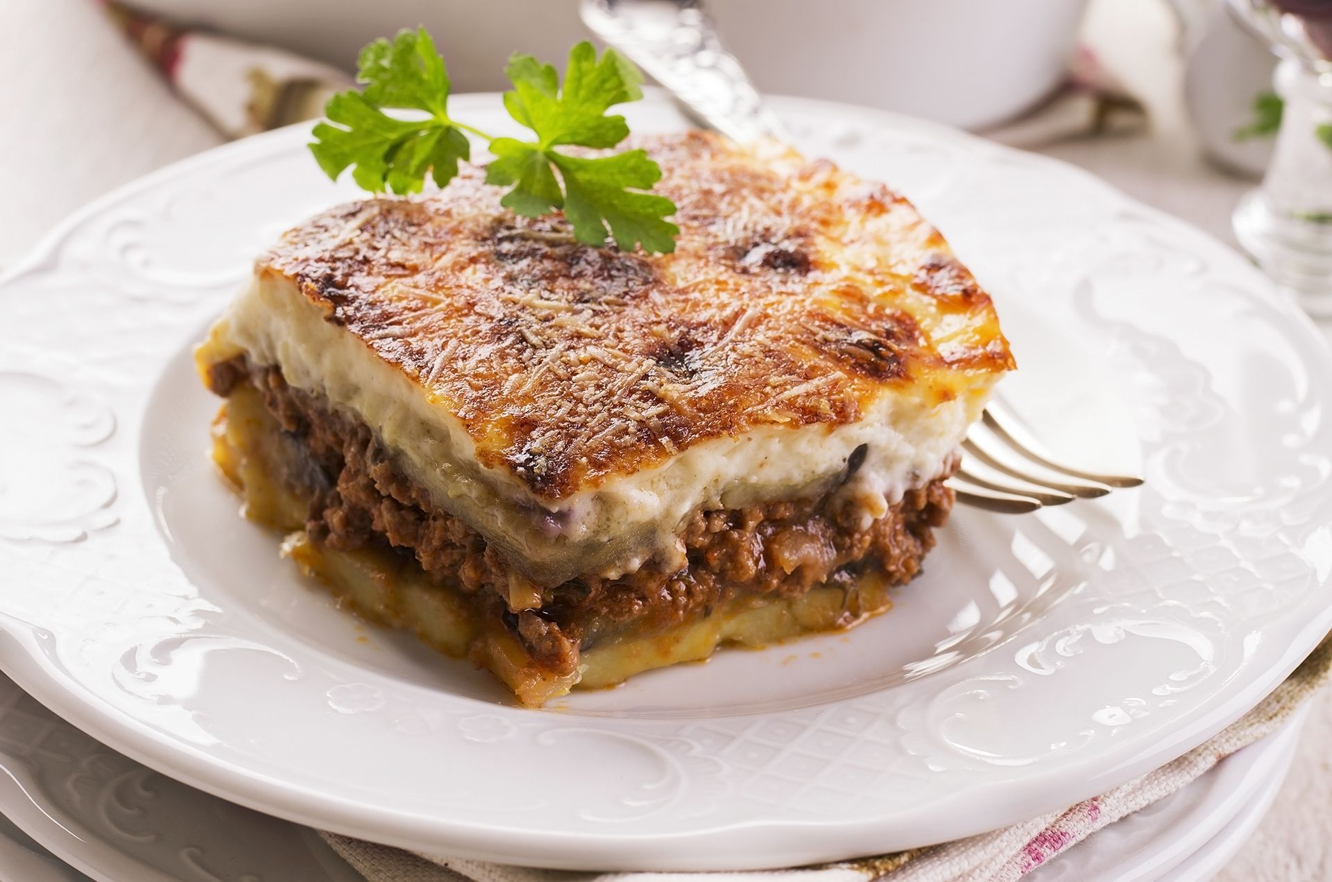 A white plate topped with a slice of lasagna and a fork