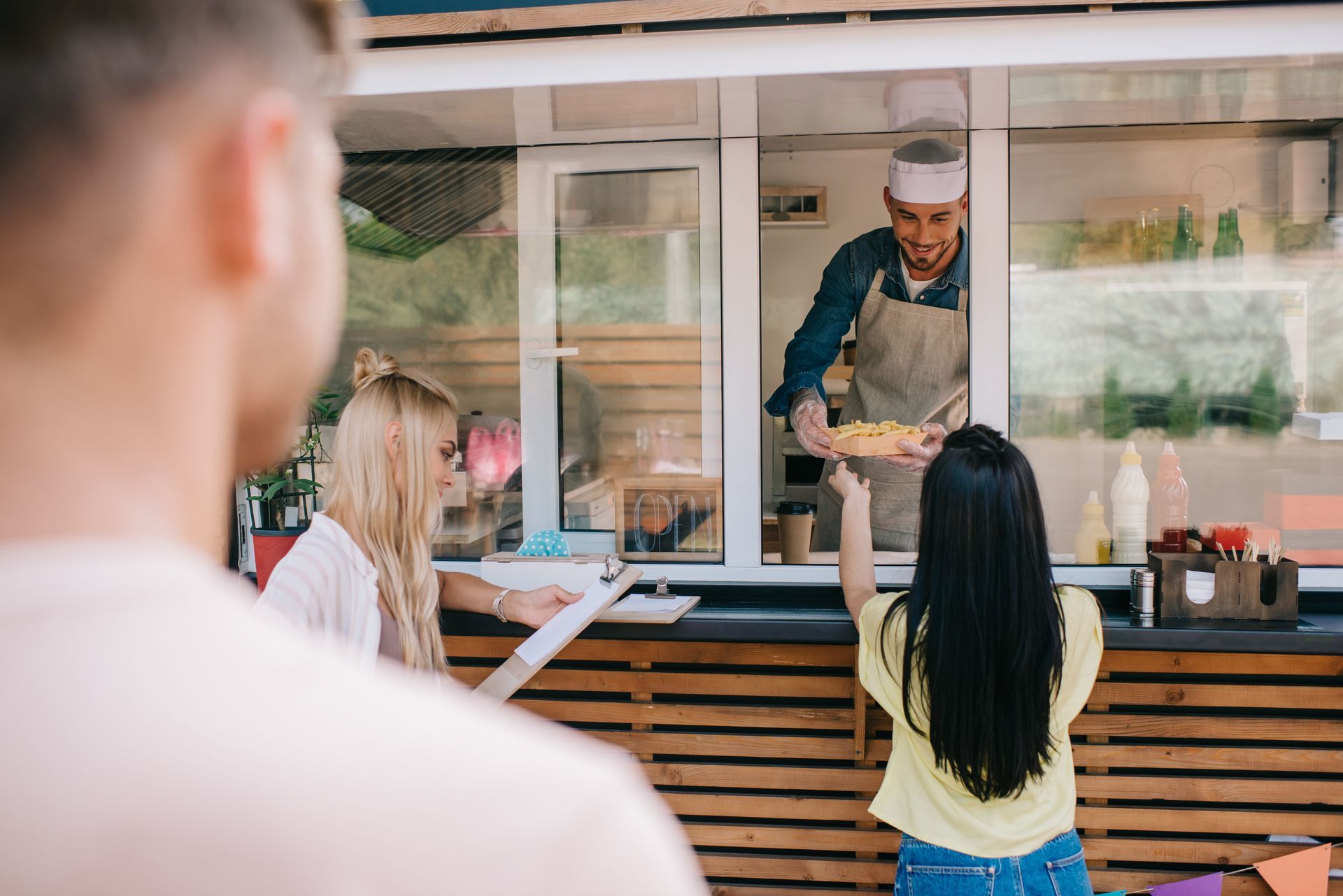 Food truck worker hands a plate of food to a customer, two other people look on.